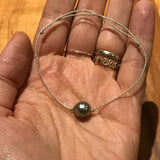 Perle de tahiti montée sur un cordon de tissu argenté japonais. Bracelet féminin et lumineux ajustable en taille.